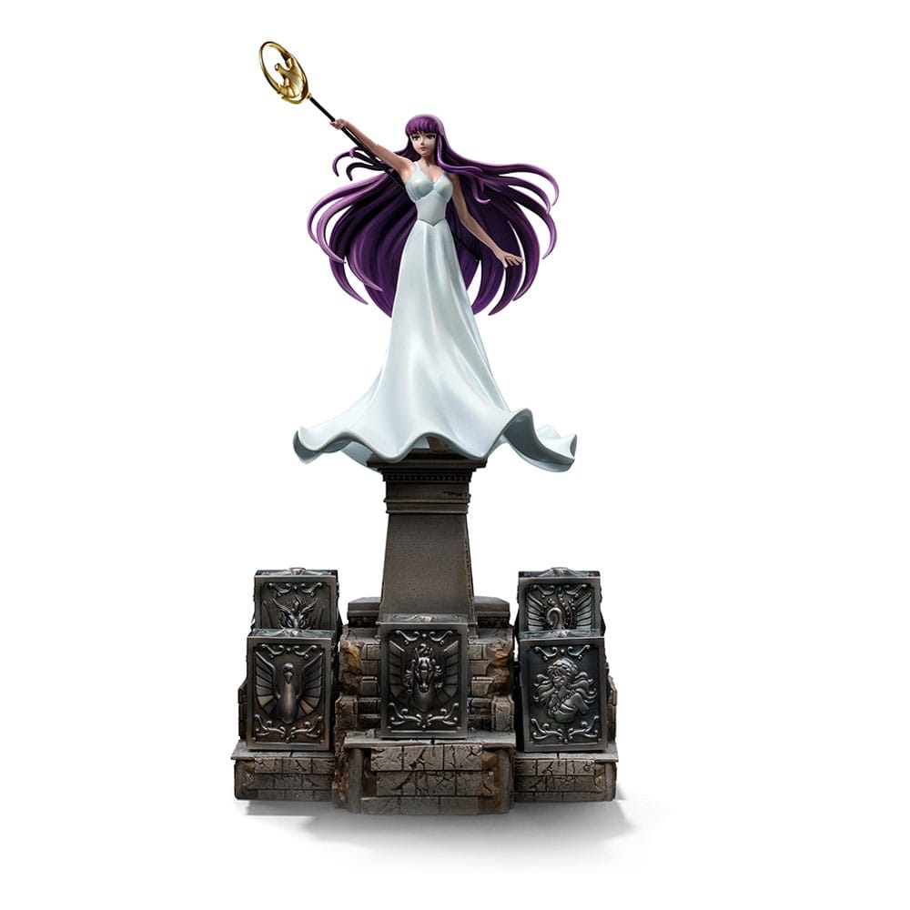 SAORI KIDO SAINT SEIYA ART SCALE 1/10. Iron Studios presenta con orgullo la estatua "Saori Kido Athena Deluxe – Saint Seiya – Art Scale 1/10", una exquisita representación de la diosa Atenea reencarnada en la icónica serie "Saint Seiya". Esta impresionante y detallada estatua pintada a mano captura a Saori Kido en toda su gracia y dignidad. De pie sobre un altar de hormigón, esta joven de figura esbelta y curva, de largo cabello morado, sostiene en el aire su bastón sagrado. Lleva un vestido largo blanco y muestra un rostro tranquilo y sereno. Debajo de sus pies, en los escalones milenarios de su santuario, se encuentran cinco Cajas de Pandora de los Santos de Bronce: Pegaso, Cisne, Dragón, Andrómeda y Fénix, que contienen las poderosas Telas. Esta pieza exclusiva de edición limitada, realizada en polystone, es una verdadera obra de arte para fanáticos y coleccionistas de "Saint Seiya".