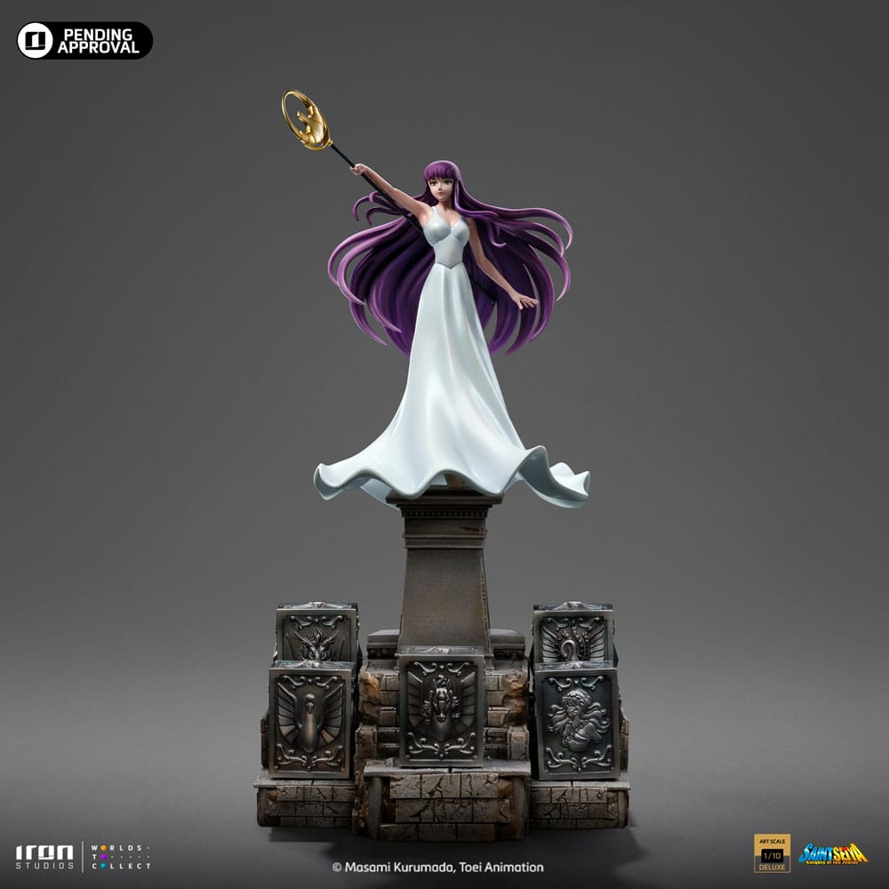 SAORI KIDO SAINT SEIYA ART SCALE 1/10. Iron Studios presenta con orgullo la estatua "Saori Kido Athena Deluxe – Saint Seiya – Art Scale 1/10", una exquisita representación de la diosa Atenea reencarnada en la icónica serie "Saint Seiya". Esta impresionante y detallada estatua pintada a mano captura a Saori Kido en toda su gracia y dignidad. De pie sobre un altar de hormigón, esta joven de figura esbelta y curva, de largo cabello morado, sostiene en el aire su bastón sagrado. Lleva un vestido largo blanco y muestra un rostro tranquilo y sereno. Debajo de sus pies, en los escalones milenarios de su santuario, se encuentran cinco Cajas de Pandora de los Santos de Bronce: Pegaso, Cisne, Dragón, Andrómeda y Fénix, que contienen las poderosas Telas. Esta pieza exclusiva de edición limitada, realizada en polystone, es una verdadera obra de arte para fanáticos y coleccionistas de "Saint Seiya".