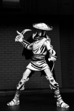 ELITE FOOT NINJA GUARD BLACK AND WHITE TEENAGE MUTANT NINJA TURTLES NECA. Basado en los cómics originales de Eastman & Laird de las Tortugas Ninja Adolescentes Mutantes de Mirage Studios.  Regresa a lo básico con la Guardia de Élite de Shredder, tal como apareció originalmente en la publicación en blanco y negro de Mirage Comics.  La Guardia de Élite, la más letal de los ninjas del Pie, está unida por honor a Shredder y es entrenada personalmente por él. Esta figura de acción mide 18 cm e incluye manos adicionales, lanza, sombrero y capa extraíble.  Viene en una caja con ventana especial con temática de cómic, ilustrada por Kevin Eastman.