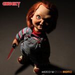 TALKING SNEERING CHUCKY CHILD’S PLAY. Mezco Toyz reincorpora a su colección MDS Mega Scale, esta figura parlante de Chucky en su versión más limpia y clásica, antes de que las cicatrices y el daño marcaran su rostro en las películas de la saga "Child’s Play" ("Muñeco diabólico" en España). Esta versión muestra a Chucky con su característico conjunto de los Good Guys, sin cortes ni desgastes, tal como sus primeras apariciones en pantalla. Mide 38 cm de alto, presenta 11 puntos de articulación, ojos con acabado vítreo realista y cabello naranja sintético. Viste ropa de tela auténtica y está equipada con un mecanismo de voz que reproduce en inglés varias frases icónicas del personaje, desde su famoso "My name is Chucky" hasta otras más siniestras.