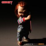 TALKING SNEERING CHUCKY CHILD’S PLAY. Mezco Toyz reincorpora a su colección MDS Mega Scale, esta figura parlante de Chucky en su versión más limpia y clásica, antes de que las cicatrices y el daño marcaran su rostro en las películas de la saga "Child’s Play" ("Muñeco diabólico" en España). Esta versión muestra a Chucky con su característico conjunto de los Good Guys, sin cortes ni desgastes, tal como sus primeras apariciones en pantalla. Mide 38 cm de alto, presenta 11 puntos de articulación, ojos con acabado vítreo realista y cabello naranja sintético. Viste ropa de tela auténtica y está equipada con un mecanismo de voz que reproduce en inglés varias frases icónicas del personaje, desde su famoso "My name is Chucky" hasta otras más siniestras.