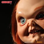 TALKING SNEERING CHUCKY CHILD’S PLAY. Mezco Toyz reincorpora a su colección MDS Mega Scale, esta figura parlante de Chucky en su versión más limpia y clásica, antes de que las cicatrices y el daño marcaran su rostro en las películas de la saga "Child’s Play" ("Muñeco diabólico" en España). Esta versión muestra a Chucky con su característico conjunto de los Good Guys, sin cortes ni desgastes, tal como sus primeras apariciones en pantalla. Mide 38 cm de alto, presenta 11 puntos de articulación, ojos con acabado vítreo realista y cabello naranja sintético. Viste ropa de tela auténtica y está equipada con un mecanismo de voz que reproduce en inglés varias frases icónicas del personaje, desde su famoso "My name is Chucky" hasta otras más siniestras.
