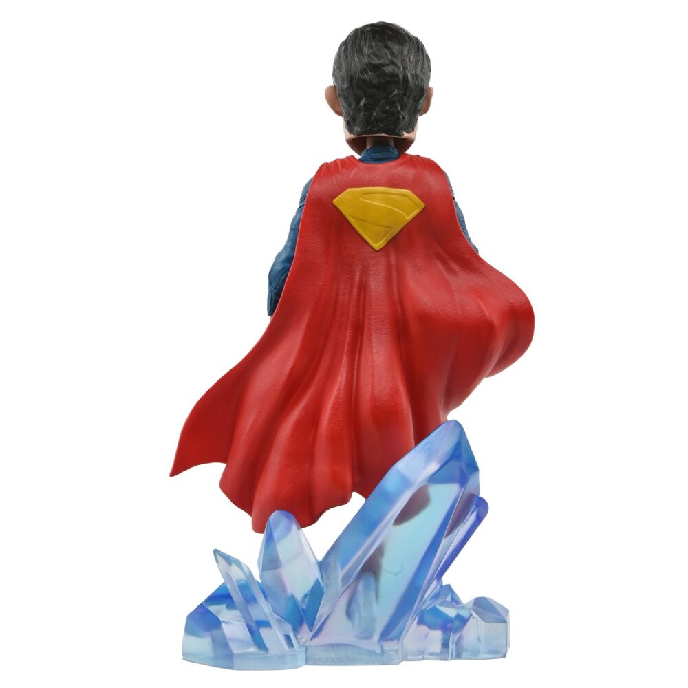 Superman 2025 dc universe head knocker. Neca presenta la figura de superman basada en el protagonista de la película homónima de 2025. Se muestra sobre una base translúcida de cristales de la fortaleza de la soledad, con su clásico traje azul y capa roja. Mide 21,5 cm, está fabricada con resina y pintada a mano con gran nivel de detalle. Cuenta con un mecanismo de resorte que permite el característico movimiento de cabeza de las figuras de la colección head knocker.