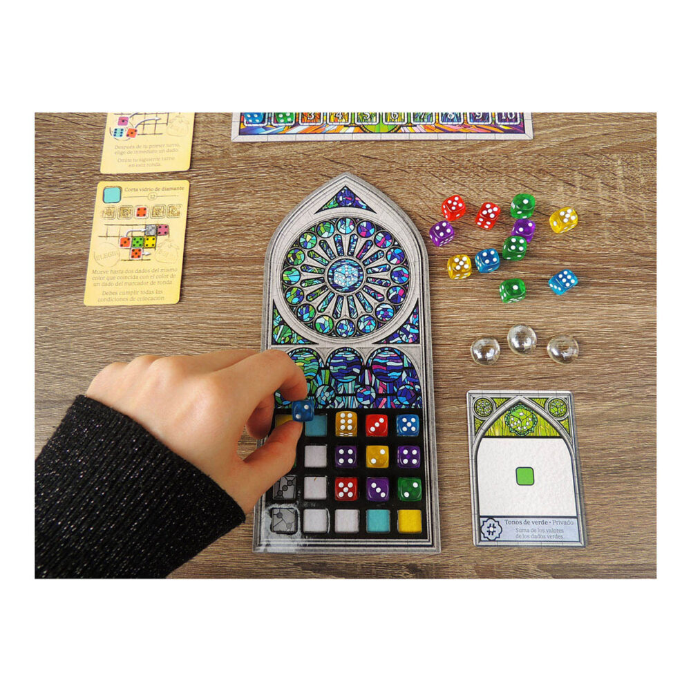 Sagrada. Es un juego de mesa abstracto, en el que los jugadores tomarán el papel de artistas creadores de vitrales que intentarán producir la pieza más hermosa para exhibirla en el templo expiatorio de la sagrada familia de antoni gaudí. Como artistas, manipularemos piezas de vidrio, que en este juego se representan con dados de diferentes colores y grados de opacidad, indicados por el valor del dado, cuanto más bajo sea su valor, menor será su opacidad.   al inicio del juego tendremos que elegir de manera aleatoria dos cartas de patrón y un tablero de marco. De las dos cartas de patrón se elige una, que se emplea durante toda la partida y se intentará completar, mientras que la otra se descarta. Este patrón marca algunas opacidades y número de dado que tendremos que conseguir. También, en la parte inferior, se indica su nivel de dificultad, que nos dará útiles fichas de donativos para poder pagar el uso de las cartas de herramienta del juego y que nos ayudarán a modificar restricciones de las reglas. Al inicio de cada partida de sagrada se colocarán los 90 dados en la bolsa, se elegirá al azar el jugador inicial, que será quien saque de la bolsa, sin mirar, una cantidad de dados igual al doble de jugadores más uno (por ejemplo, si hay 2 jugadores sacaremos 5 dados). La partida se desarrolla en el sentido de las manecillas del reloj y cada jugador puede llevar a cabo las siguientes acciones en cualquier orden: elegir un dado y colocarlo en su vitral teniendo en cuenta que debe estar adyacente a otros dados, usar una carta de herencia pagando su coste en donativos, o pasar un turno sin realizar acciones. Tras el turno del último jugador sigue la ronda, pero en sentido contrario, y los dados restantes van al marcador de ronda, hasta jugar un total de 10 rondas.. Sagrada se puede jugar en modo solitario o con hasta cuatro jugadores, en partidas que duran de 30 a 45 minutos. Es ideal para los amantes de los juegos abstractos como los sudokus o los rompecabezas, ya que intentar armar los patrones con todas las restricciones aplicadas les proporcionará muchas partidas llenas de diversión. Conviértete en un artista del vitral en sagrada, demuestra que eres quien tienes las mejores dotes artísticas y crea la mejor obra de arte para ser exhibida en el templo de la sagrada familia en este juego abstracto de colocación de dados.  consíguelo en tu tienda especializada en juegos de mesa favorita.