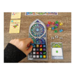 SAGRADA. Es un juego de mesa abstracto, en el que los jugadores tomarán el papel de artistas creadores de vitrales que intentarán producir la pieza más hermosa para exhibirla en el Templo Expiatorio de la Sagrada Familia de Antoni Gaudí. Como artistas, manipularemos piezas de vidrio, que en este juego se representan con dados de diferentes colores y grados de opacidad, indicados por el valor del dado, cuanto más bajo sea su valor, menor será su opacidad.  Al inicio del juego tendremos que elegir de manera aleatoria dos cartas de patrón y un tablero de marco. De las dos cartas de patrón se elige una, que se emplea durante toda la partida y se intentará completar, mientras que la otra se descarta. Este patrón marca algunas opacidades y número de dado que tendremos que conseguir. También, en la parte inferior, se indica su nivel de dificultad, que nos dará útiles fichas de donativos para poder pagar el uso de las cartas de herramienta del juego y que nos ayudarán a modificar restricciones de las reglas. Al inicio de cada partida de Sagrada se colocarán los 90 dados en la bolsa, se elegirá al azar el jugador inicial, que será quien saque de la bolsa, sin mirar, una cantidad de dados igual al doble de jugadores más uno (por ejemplo, si hay 2 jugadores sacaremos 5 dados). La partida se desarrolla en el sentido de las manecillas del reloj y cada jugador puede llevar a cabo las siguientes acciones en cualquier orden: elegir un dado y colocarlo en su vitral teniendo en cuenta que debe estar adyacente a otros dados, usar una carta de herencia pagando su coste en donativos, o pasar un turno sin realizar acciones. Tras el turno del último jugador sigue la ronda, pero en sentido contrario, y los dados restantes van al marcador de ronda, hasta jugar un total de 10 rondas.. Sagrada se puede jugar en modo solitario o con hasta cuatro jugadores, en partidas que duran de 30 a 45 minutos. Es ideal para los amantes de los juegos abstractos como los sudokus o los rompecabezas, ya que intentar armar los patrones con todas las restricciones aplicadas les proporcionará muchas partidas llenas de diversión. Conviértete en un artista del vitral en Sagrada, demuestra que eres quien tienes las mejores dotes artísticas y crea la mejor obra de arte para ser exhibida en el templo de la Sagrada Familia en este juego abstracto de colocación de dados. Consíguelo en tu tienda especializada en juegos de mesa favorita.