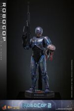ROBOCOP 2 MOVIE MASTERPIECE HOT TOYS 1/6. Es considerada una película clásica de acción y ciencia ficción, muy querida por muchos fans. La historia sigue a RoboCop, un agente de la ley cíborg que antes era un humano llamado Alex Murphy. Tras ser brutalmente asesinado en acto de servicio, se transforma en un poderoso robot de alta tecnología con habilidades avanzadas. Posee superfuerza, visión mejorada y un compromiso inquebrantable con la ley. En "RoboCop 2", RoboCop continúa protegiendo a los ciudadanos de Detroit. Se enfrenta a una nueva amenaza cuando un ejecutivo rebelde de OCP desarrolla una versión más avanzada y malévola de RoboCop, lo que supone un grave desafío para su misión y la seguridad de la ciudad.