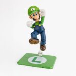LUIGI SUPER MARIO SH FIGUARTS.Tamashii suma a su colección S.H. Figuarts esta figura articulada de Luigi, basada en su personaje en la serie de videojuegos "Super Mario Bros". Con una altura aproximada de 11 cm, está diseñada para capturar sus características y variadas poses. Incluye 1x bloque de ladrillos, 1x caparazón rojo Akakora, 1x base de exhibición especial con su emblema, 2x manos intercambiables y 1x set de piezas de articulación para el caparazón rojo. Fabricada en ABS/PVC.