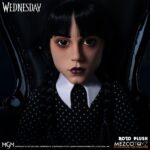 WEDNESDAY MDS ROTO PLUSH. Mezco suma a su línea MDS Roto Plush la figura de Wednesday Addams (conocida como Miércoles Addams en España), inspirada en la exitosa serie de Netflix "Wednesday". Tiene una altura aproximada de 45 cm. Se muestra con su característico gesto serio, un vestido negro manga larga con cuello alto, sus clásicas trenzas de cabello negro implantadas y zapatos al estilo Mary Jane. Cuenta con partes esculpidas sobre un cuerpo de felpa. Se presenta en una caja con ventana