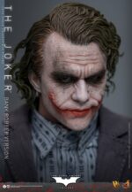 THE JOKER (BANK ROBBER VERSION) THE DARK KNIGHT HOT TOYS 1/6. El Joker de Heath Ledger conmocionó al mundo mucho antes de que se disparara la primera bala. Su risa escalofriante y sus acciones caóticas lo han convertido en un verdadero ícono del cine. La escena del robo al banco en Batman: El Caballero de la Noche sirve como una introducción cautivadora a la encantadora interpretación del Joker por parte de Ledger y define el tono del personaje. Hoy, Hot Toys se complace en presentar la figura coleccionable a escala 1/6 del Joker (versión ladrón de bancos), que ofrece una versión pulida y auténtica del icónico Joker del robo al banco de Ledger. Incluye dos cabezas detalladas con ojos giratorios separados, una con la siniestra sonrisa del Joker y otra con la máscara de payaso de ladrón de bancos. La figura captura la imagen del Joker del inolvidable atraco inicial al banco de El Caballero de la Noche. La figura incluye cabello verde oscuro de longitud media y texturas de piel finamente pintadas, incluyendo arrugas y manchas de maquillaje que recuerdan a la película. El atuendo de ladrón de bancos está meticulosamente confeccionado, con una camisa a rayas bajo un blazer y pantalones grises.
