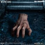 WEDNESDAY LIVING DEAD DOLLS MEZCO. Mezco Toyz vuelve a presentar dentro de su línea Living Dead Dolls la muñeca de Wednesday Addams, inspirada en la serie de Netflix "Wednesday" ("Miércoles" en España). La figura mide aproximadamente 25 cm de altura, cuenta con 5 puntos de articulación y se muestra con su característico vestido negro con cuello, mallas oscuras y botas. Luce su peinado clásico con coletas y un nuevo esculpido facial. Como accesorio se incluye su inseparable mano sirviente Cosa en pose estática. Se presenta en una caja con ventana.