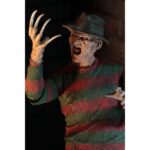 ULTIMATE FREDDY KRUEGER A NIGHTMORE ON ELM STREET PART 2. Neca vuelve a añadir a su línea Ultimate la figura de Freddy Krueger basada en la película "A Nightmare on Elm Street Part 2: Freddy's Revenge" ("Pesadilla en Elm Street 2: La venganza de Freddy" en España). Mide 18 cm e incluye 3x cabezas intercambiables, 2x perros demoníacos, 1x mano enguantada, 1x mano afilada, 1x sombrero extraíble y 1x efecto de fuego magnético. Se presenta en una caja con ventana y solapa frontal.