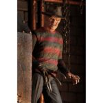 ULTIMATE FREDDY KRUEGER A NIGHTMORE ON ELM STREET PART 2. Neca vuelve a añadir a su línea Ultimate la figura de Freddy Krueger basada en la película "A Nightmare on Elm Street Part 2: Freddy's Revenge" ("Pesadilla en Elm Street 2: La venganza de Freddy" en España). Mide 18 cm e incluye 3x cabezas intercambiables, 2x perros demoníacos, 1x mano enguantada, 1x mano afilada, 1x sombrero extraíble y 1x efecto de fuego magnético. Se presenta en una caja con ventana y solapa frontal.