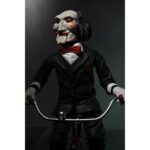 BILLY THE PUPPET ON TRICYCLE SAW 12″. Neca reincorpora en su catálogo esta figura de 30 cm de Billy the Puppet, el siniestro muñeco de la saga "Saw". Se muestra montado en su icónico triciclo rojo con zapatos de purpurina e incluye función de sonido con frases de la película. Emplea 3 baterías de 1.5V LR44 (incluidas). Se presenta en una caja con ventana.