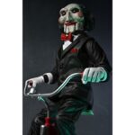 BILLY THE PUPPET ON TRICYCLE SAW 12″. Neca reincorpora en su catálogo esta figura de 30 cm de Billy the Puppet, el siniestro muñeco de la saga "Saw". Se muestra montado en su icónico triciclo rojo con zapatos de purpurina e incluye función de sonido con frases de la película. Emplea 3 baterías de 1.5V LR44 (incluidas). Se presenta en una caja con ventana.