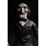 BILLY THE PUPPET ON TRICYCLE SAW 12″. Neca reincorpora en su catálogo esta figura de 30 cm de Billy the Puppet, el siniestro muñeco de la saga "Saw". Se muestra montado en su icónico triciclo rojo con zapatos de purpurina e incluye función de sonido con frases de la película. Emplea 3 baterías de 1.5V LR44 (incluidas). Se presenta en una caja con ventana.