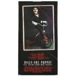BILLY THE PUPPET ON TRICYCLE SAW 12″. Neca reincorpora en su catálogo esta figura de 30 cm de Billy the Puppet, el siniestro muñeco de la saga "Saw". Se muestra montado en su icónico triciclo rojo con zapatos de purpurina e incluye función de sonido con frases de la película. Emplea 3 baterías de 1.5V LR44 (incluidas). Se presenta en una caja con ventana.