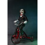 BILLY THE PUPPET ON TRICYCLE SAW 12″. Neca reincorpora en su catálogo esta figura de 30 cm de Billy the Puppet, el siniestro muñeco de la saga "Saw". Se muestra montado en su icónico triciclo rojo con zapatos de purpurina e incluye función de sonido con frases de la película. Emplea 3 baterías de 1.5V LR44 (incluidas). Se presenta en una caja con ventana.