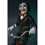BILLY THE PUPPET ON TRICYCLE SAW 12″. Neca reincorpora en su catálogo esta figura de 30 cm de Billy the Puppet, el siniestro muñeco de la saga "Saw". Se muestra montado en su icónico triciclo rojo con zapatos de purpurina e incluye función de sonido con frases de la película. Emplea 3 baterías de 1.5V LR44 (incluidas). Se presenta en una caja con ventana.