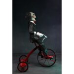 BILLY THE PUPPET ON TRICYCLE SAW 12″. Neca reincorpora en su catálogo esta figura de 30 cm de Billy the Puppet, el siniestro muñeco de la saga "Saw". Se muestra montado en su icónico triciclo rojo con zapatos de purpurina e incluye función de sonido con frases de la película. Emplea 3 baterías de 1.5V LR44 (incluidas). Se presenta en una caja con ventana.