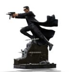 NEO THE MATRIX ART SCALE 1/10. Directamente desde una escena icónica de Matrix, Neo se lanza al aire, con su gabardina ondeando y las armas desenfundadas, desafiando la gravedad y enfrentándose a lo imposible. Esta figura lo captura en pleno salto, congelado en el momento en que las balas vuelan y el tiempo se ralentiza. Es la esencia de Matrix en una sola pose. Como héroe legendario de la trilogía, Neo simboliza la rebelión, la duda y, finalmente, la fe absoluta. Esta escultura lo captura en un momento decisivo: concentrado, en el aire y con el control absoluto. Su gabardina ondeando, sus gafas oscuras y su expresión estoica son un guiño al lenguaje visual que lo convirtió en un icono cinematográfico. La base representa una pared derruida en medio de un tiroteo: agujeros de bala, fragmentos de yeso y cables rotos. Los efectos de polvo esculpidos añaden movimiento dinámico a la escena. El marcado contraste entre su traje negro y los escombros de hormigón realza el dramatismo de la figura. Fabricada en resina y con una altura aproximada de 25 cm a escala 1/10, esta pieza forma parte de la línea Art Scale de Iron Studios, conocida por sus poses cinematográficas y sus detalles realistas. Imprescindible para los fans de Matrix y los coleccionistas de cultura pop que buscan impacto visual.