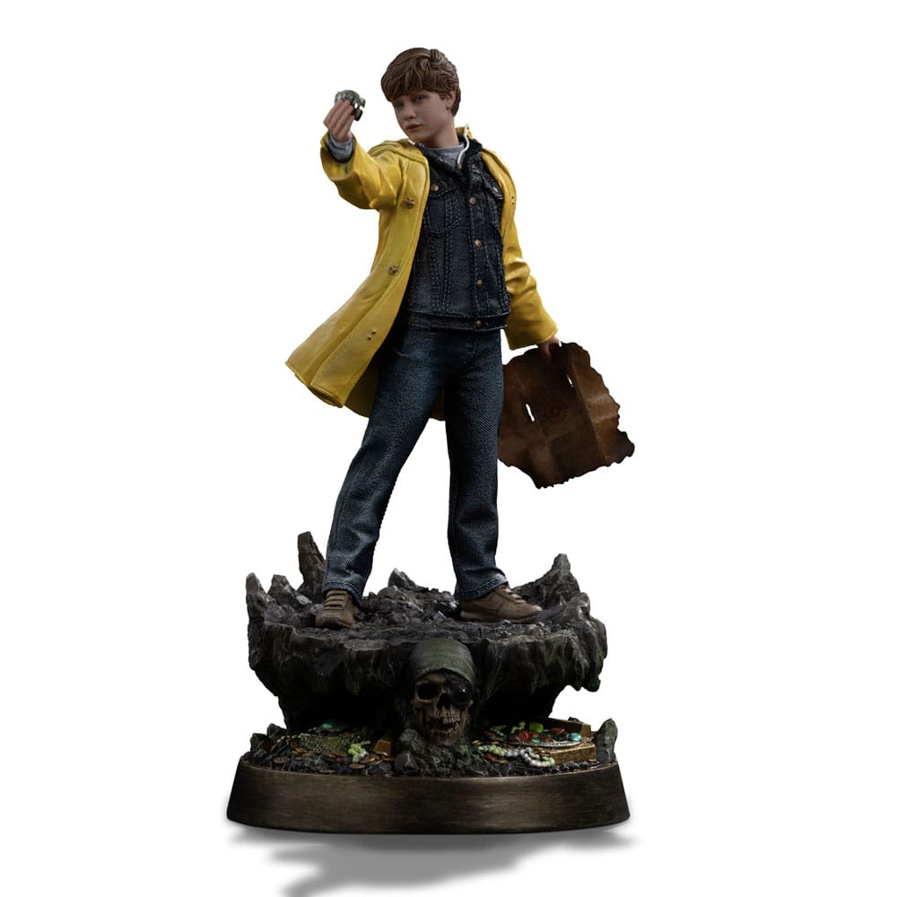 MIKEY WALSH (40TH ANNIVERSARY) THE GOONIES ART SCALE 1/10. Mikey Walsh regresa en esta figura conmemorativa del 40 aniversario de Los Goonies, capturando la energía y la determinación del valiente joven líder. De pie sobre una base con forma de cueva pirata, con un mapa del tesoro en una mano y una moneda de oro en la otra, encarna a la perfección el espíritu de la aventura infantil: misterio, valentía e imaginación. Como líder natural de la pandilla, Mikey puede que no tenga poderes ni equipo, pero lidera con esperanza y lealtad. Su pose, con la mirada puesta en el futuro, refleja ese momento icónico en el que la historia se hace realidad y los niños se convierten en héroes. La moneda que sostiene en la mano conecta el mito con la acción, la esperanza con el descubrimiento. La escultura recrea fielmente su icónico aspecto: impermeable amarillo brillante, camisa vaquera, pantalones vaqueros y zapatillas gastadas. La base está ricamente detallada, con texturas de roca, monedas de oro, reliquias antiguas y una calavera tallada, lo que evoca instantáneamente la atmósfera de la búsqueda subterránea de la película. Fabricada en resina a escala 1/10, la estatua mide aproximadamente 21 cm de altura. Forma parte de la colección Art Scale de Iron Studios, que se centra en la nostalgia y los detalles. Una pieza central perfecta para los fans de Los Goonies, o para cualquiera que todavía crea en los tesoros enterrados y las aventuras con los mejores amigos.