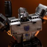 MEGATRON TRANSFORMERS DEMI ART SCALE 1/10. Encarnación de la estrategia despiadada y el poder bruto, Megatron se yergue imponente en esta pose dominante sobre los restos humeantes de sus enemigos. Inspirada en el universo clásico de Transformers, esta figura de resina captura el frío dominio y la presencia icónica del líder Decepticon. Con el cañón de fusión apuntando y listo, la mirada de Megatron se fija en su objetivo con una confianza inquebrantable. Su diseño retrofuturista —chapa metálica cepillada, estructura angular, detalles tecnológicos desgastados— se recrea con una precisión sorprendente. La base representa un campo de batalla en llamas: robots destrozados, cables rotos, llamas esculpidas y efectos de humo realzan la intensidad de la escena. El cañón brillante y aún humeante añade una dramática sensación de acción reciente. Fabricada en resina y con una altura aproximada de 32 cm a escala 1/20, esta estatua pertenece a la línea Demi Art Scale de Iron Studios. Ofrece texturas nítidas, una pose audaz y una base narrativa que realza toda la pieza. Una representación feroz e inolvidable de Megatron, perfecta para los fans que quieren que su exposición irradie amenaza.