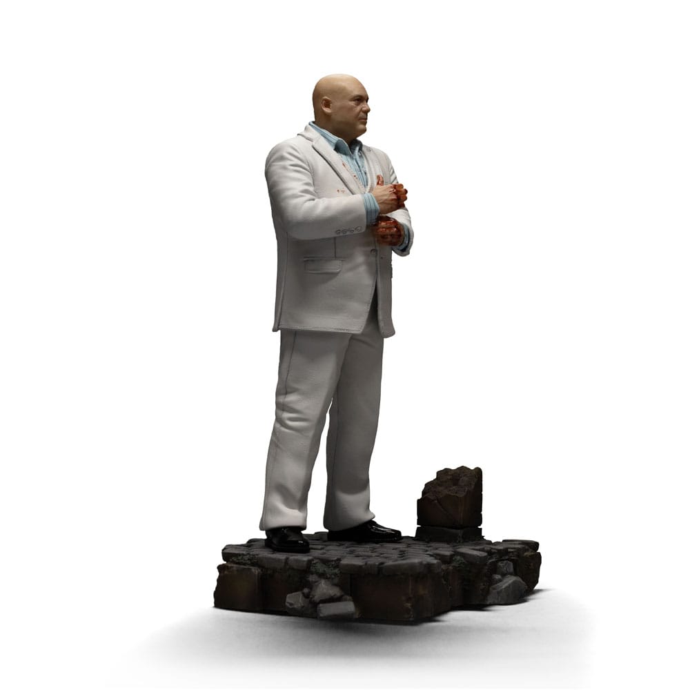 KINGPIN DAREDEVIL: BORN AGAIN ART SCALE 1/10. En el oscuro y urbano universo de Marvel, Wilson Fisk, alias Kingpin, reina sobre el crimen organizado con una inteligencia fría y mano de hierro. Enemigo emblemático de Daredevil, encarna la corrupción arraigada en las calles de Hell's Kitchen, utilizando su influencia política y su fuerza bruta para afianzar su poder. Aquí representado de pie en una postura imponente, Kingpin sujeta su bastón con calma y seguridad. Su mirada dura y su estatura imponente transmiten una autoridad indiscutible. Su atuendo, un traje blanco perfectamente cortado, contrasta con la atmósfera amenazante que lo rodea, lo que subraya su gusto por el control y la puesta en escena. Cada detalle visual está cuidadosamente trabajado: cabeza rapada, rasgos cerrados, camisa azul pálida y bastón esculpido. La base imita un adoquín urbano roto, acentuando el contraste entre su aparente elegancia y la brutalidad de su entorno. El realismo de los pliegues de la tela y la textura de la base aportan profundidad y presencia a esta pieza. Fabricada en resina, esta figura mide aproximadamente 21 cm y está diseñada a escala 1/10. Forma parte de la colección Art Scale de Iron Studios y se apoya en una base detallada, lista para completar una escena realista de Marvel o para presidir por sí sola como representación de uno de los antagonistas más poderosos del universo.