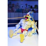 STUMP WRESTLING ACE DUCK TEENAGE MUTANT NINJA TURTLES ARCHIE COMICS. Ace Duck, personaje secundario de culto del universo Tortugas Ninja, reaparece aquí en su versión Stump Wrestling, inspirada en los famosos combates intergalácticos del multiverso TMNT. Este carismático luchador antropomórfico adopta aquí el aspecto de un guerrero samurái, listo para luchar en la arena con estilo y poderío. La figura representa a Ace Duck con un atuendo inspirado en el Japón feudal, con un kimono azul y negro, un cinturón rojo atado a la cintura y una espada enfundada. Su complexión robusta está perfectamente representada, con brazos musculosos, patas palmeadas y un feroz rostro de pato con colmillos visibles. Todo ello se acentúa con una capa de tela marrón y una variedad de accesorios evocadores. El conjunto incluye varias manos intercambiables, una antorcha esculpida, un escudo redondo y una gran capa flexible para variar las poses. Los detalles están cuidados al máximo: nervaduras en las alas, texturas del kimono, funda realista. La articulación fluida permite colocarlo en poses de combate o de parada. Con sus 18 cm, esta figura de NECA combina un guiño retro con una ejecución moderna. Una pieza ideal para los coleccionistas de la gama TMNT que quieran enriquecer su exposición con variantes originales y cuidadas.