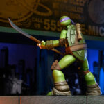 ULTIMATE DONATELLO TEENAGE MUTANT NINJA TURTLES (2012). En la serie animada Teenage Mutant Ninja Turtles de 2012, Donatello es el cerebro técnico del equipo. Aborda cada situación con precisión, equilibrando inventos, improvisación y un profundo sentido de la responsabilidad. Su mentalidad tranquila y lógica mantiene al grupo con los pies en la tierra mientras sus hermanos se lanzan al ataque. A lo largo de la serie, Donnie es a menudo quien idea soluciones cuando las cosas se complican. Ya sea construyendo nuevos equipos, analizando amenazas u ofreciendo un apoyo silencioso, se erige como la fuerza estabilizadora y el solucionador de problemas del equipo. La figura captura con precisión su aspecto de 2012: caparazón beige y marrón, piel verde, máscara morada y almohadillas de armadura marrones. Su expresión neutra se complementa con una cara alternativa más expresiva. El conjunto de accesorios es muy completo e incluye bastones segmentados, artilugios, manos intercambiables, visera tecnológica, porción de pizza, huevo, pieza de armadura e incluso un pollo mutante sacado directamente de la serie. El esculpido nítido, la aplicación limpia de la pintura y las articulaciones bien integradas realzan la presencia de la figura. Con 18 cm de altura, ofrece una articulación sólida para posar de forma dinámica y recrear escenas de la serie.