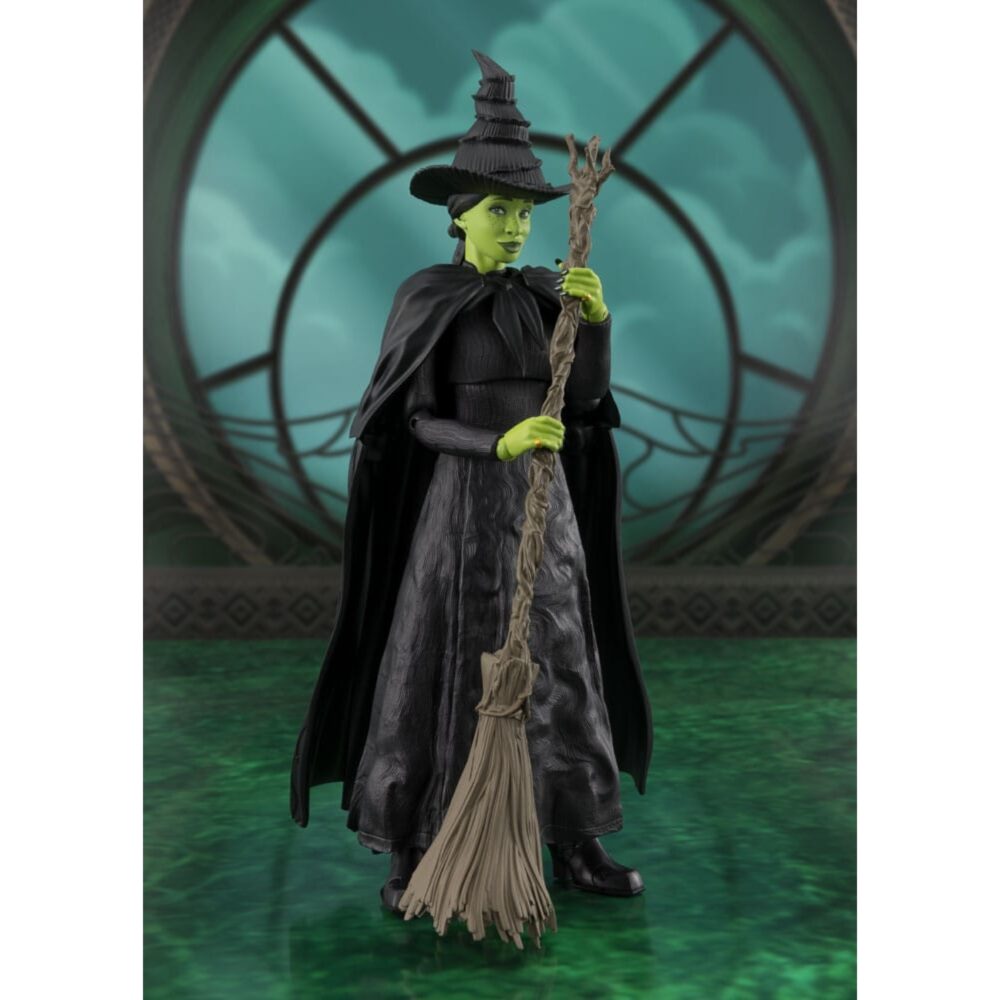 ELPHABA WICKED SH FIGUARTS. Inspirada en el musical de culto Wicked, esta figura captura toda la misteriosa intensidad de Elphaba, la bruja con un destino adverso. En un mundo en el que la apariencia y la verdad se enfrentan, ella se enfrenta con orgullo a los prejuicios y las manipulaciones, barriendo las convenciones con un simple hechizo. Heroína atípica y conmovedora, Elphaba encarna una resistencia interior marcada por la injusticia. Lejos de la imagen tradicional de la bruja malvada, a lo largo de la historia revela una complejidad poco común y conmovedora, lo que la convierte en uno de los personajes más fuertes y humanos de la narración. La figura la muestra de espaldas, en una postura llena de dignidad, ligeramente girada, con una escoba en la mano. Su piel verde resalta bajo la luz del atardecer, contrastando con su largo vestido negro texturizado, su sombrero puntiagudo torcido y su cabello trenzado. Cada pliegue de la tela, cada detalle del accesorio evoca un trabajo minucioso fiel al universo de la escena. Con unos 14 cm de altura, esta figura articulada de PVC pertenece a la colección S.H. Figuarts de Bandai. La delicada escultura, los efectos de textura del vestido, el realismo de la escoba y las elegantes proporciones la convierten en una pieza expresiva, perfecta para recrear escenas emblemáticas del musical.
