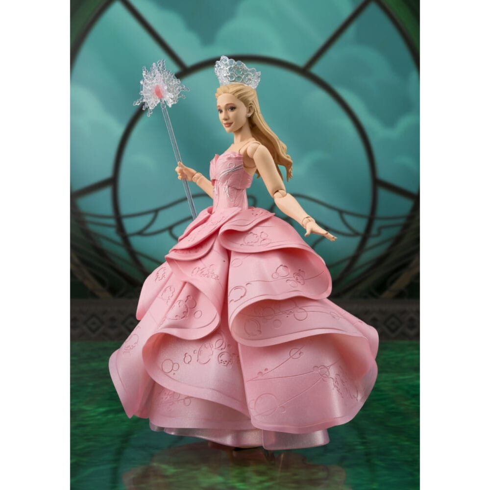 GLINDA WICKED SH FIGUARTS. Procedente directamente del encantador universo de Wicked, Glinda brilla en esta interpretación fiel y articulada. Representada en todo su esplendor, la famosa bruja del sur encarna aquí la luz, la gracia y un cierto sentido de lo espectacular, en una versión que evoca las mejores escenas del musical. Personaje en total contraste con Elphaba, Glinda desempeña un papel clave en el equilibrio narrativo de la historia. Al principio frívola y segura de sí misma, evoluciona a lo largo de la trama para revelar una personalidad más matizada, entre la ambición, la compasión y la búsqueda de identidad. La figura la muestra en plena gesticulación, con una varita mágica estrellada en la mano. Su vestido rosa con varios volantes, ricamente esculpido, presenta motivos florales en relieve. Su corona plateada, su expresión dulce y su postura grácil refuerzan la elegancia del personaje. Cada pliegue, cada nivel de la falda, da una impresión de movimiento y de escena. Con sus 15 cm de altura, esta pieza articulada de PVC forma parte de la colección S.H. Figuarts de Bandai. El trabajo en las texturas, la flexibilidad de las articulaciones y la delicadeza de los detalles (especialmente la varita y el vestido) permiten numerosas poses sin perder la estética cuidada del modelo original.
